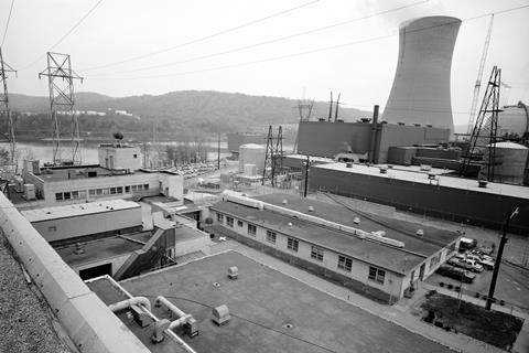 A black and white photo of an atomic power station with power lines, a cooling tower and flat-roofed buildings